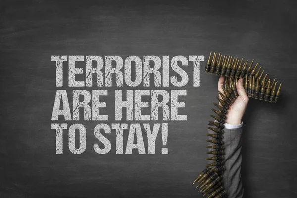 Terrorist are here to stay text on blackboard with businessman hand holding ammunition — Stock Photo, Image