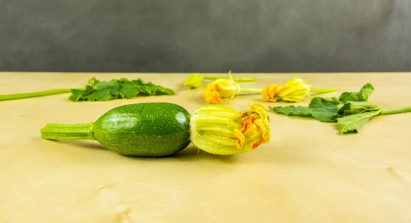Young green zucchini with a flower on the board. In the background, flowers and leaves.