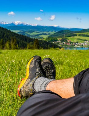 Bir hafta sonu seyahatinin zorluklarından sonra dağ sırtı ve vadideki göl manzaralı yeşil bir arazide dinlenen bir turist..