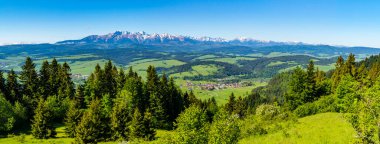 Dağ sırasının geniş bir manzarası, Tatra Dağları. Vadide ormanlar, çayırlar ve tarlalarla çevrili bir köy var. İlkbahar kırsal alanı.