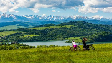 Czorsztyn, Polonya - Haziran 06, 2020: Bisikletle birkaç turist geldi. Adam dürbünden bakıyor. - Ne? Bir kadın, sosyal ağ sitelerine telefonla fotoğraf gönderiyor..