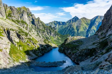 Dağ yaz manzarası. Vadinin etrafındaki kayalık duvarların oradaki gölgeli göl. Arka planda, tepelerin yeşil yamaçları. Tatry Dağları. Slovakya.