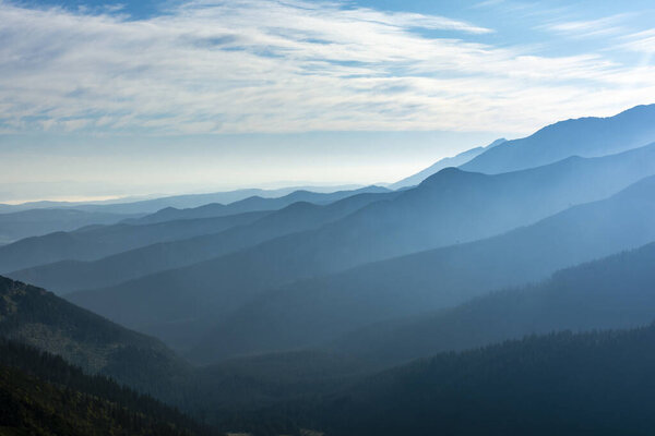 Beautiful late summer mists in the valleys between the ridges illuminated by the rays of the morning sun.