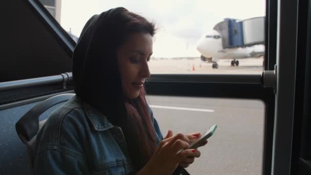 Молодая туристка смешанной расы в автобусе с помощью мобильного смартфона в аэропорту. 4K . — стоковое видео