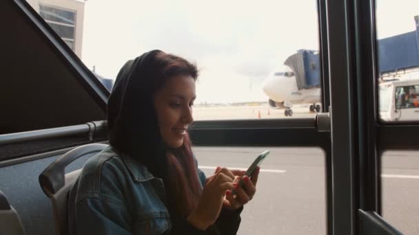 Jong gemengd ras toeristische vrouw in de Bus met behulp van mobiele slimme telefoon op luchthaven. 4k. — Stockvideo