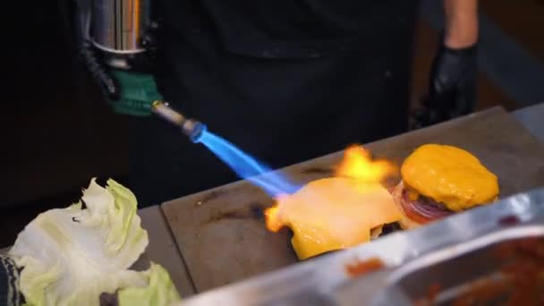 Шеф-повар плавит веганский сыр с помощью горящей пожарной плиты и делает бургер на кухне ресторана. 4K Slowmotion . — стоковое видео