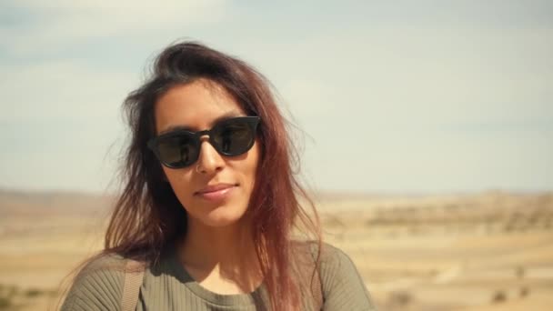 Jonge aantrekkelijke glimlachend gemengd rende meisje portret in een woestijn. Gelukkig toeristische vrouw poseren op Camera met haren wuiven in de Wind. Cappadocië, Turkije. 4k Slowmotion. — Stockvideo