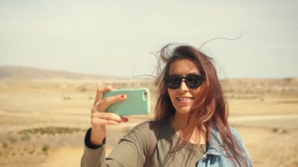 年轻迷人的微笑混合种族女孩在手机上拍摄沙漠全景照片。愉快的旅游妇女在墨镜录制视频。土耳其卡帕多西亚4k 慢动作. — 图库视频影像