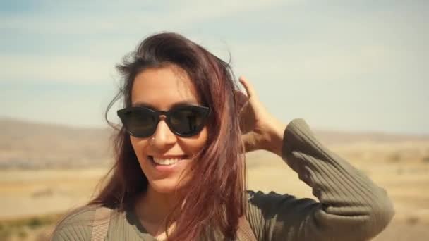 Unga attraktiva leende blandade lagerbanor flicka stående i en öken. Glad turist kvinna poserar på kamera med hår vajande i vinden. Kappadokien, Turkiet. 4k Slowmotion. — Stockvideo