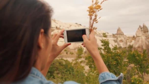 Jong gemengd ras toeristische meisje neemt foto's van prachtige berg stenen met behulp van de mobiele telefoon in Cappadocië, Turkije. 4k Slowmotion. — Stockvideo