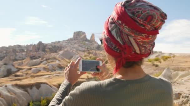 Fiatal kevert turista lány fényképez a sivatagi völgyben mobiltelefon használata. Cappadocia, Törökország. 4k. — Stock videók