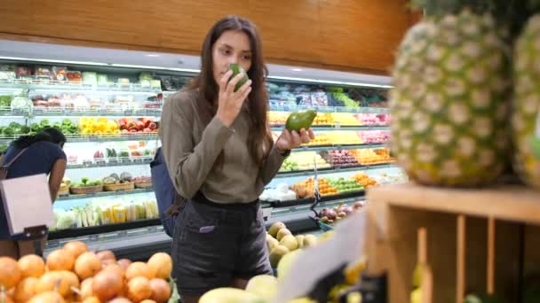 Junge Frau wählt Avocados im Lebensmittelladen. Vegane Zero-Waste-Mädchen kaufen Obst und Gemüse im Bio-Supermarkt. 4k-Zeitlupe. — Stockvideo