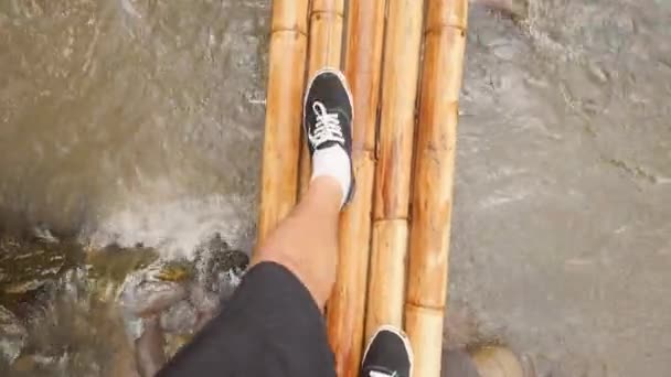 Jonge reiziger Man lopen op kleine bamboe brug Over Jungle rivier in tropisch regenwoud. 4k eerste persoon bekijken van bovenaf. Bali, Indonesië. — Stockvideo