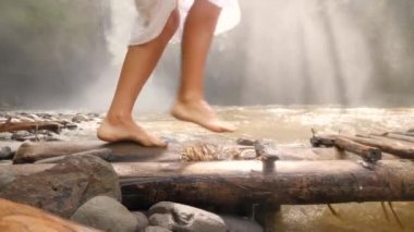 Çıplak ayakla küçük ahşap köprü üzerinde orman nehir tropikal yağmur ormanlarında yürüyüş beyaz elbiseli çekici genç kadın. 4k Slowmotion. Bali, Endonezya.