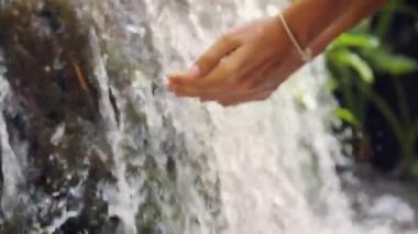 Genç kadın toplama götürdü eller taze temiz doğal kaynak suyu Jungle şelale ile. 4k Slowmotion. Bali, Endonezya.