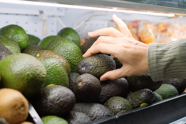 Молодая женщина выбирает авокадо в продуктовом магазине. Веганы покупают фрукты и овощи в органическом супермаркете . — стоковое фото