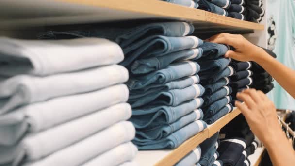 Giovane donna che prende paio di jeans blu denim da pile in negozio di abbigliamento. Mani femminili Scegliere la taglia corretta dei pantaloni nel centro commerciale. Concetto di consumo al rallentatore 4K . — Video Stock