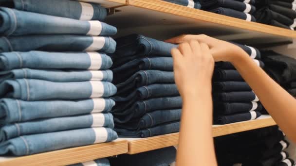 Fiatal nő vesz pár kék farmert halom ruházati üzlet. Női kezek kiválasztásánál a megfelelő nadrág méret bevásárlóközpontban. 4 k Slowmotion fogyasztás fogalmát. — Stock videók