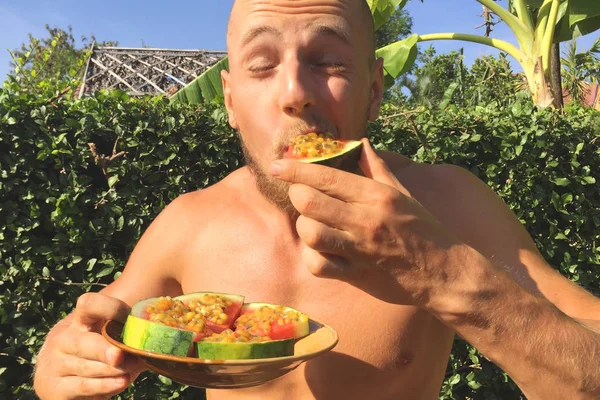 Young Athletic Vegan Guy Eating Watermelon Raw Pizza with Passion Fruit on Top. Organic Tasty Fresh Fruit Diet Breakfast. Thailand.