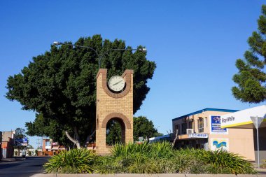 Emerald, Queensland, Avustralya - 08 / 30 / 2014; Zümrüt, Queensland 'in iş merkezinde büyük bir incir ağacı ve arka planda dükkanları olan kare tuğla saat kulesi.                              