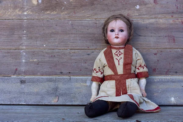 Scary creepy old vintage doll with staring eyes and plaited hair in an old dress against a rustic background with copy space.