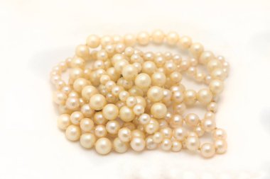 Farklı boyutlarda, beyaz arka planda istiflenmiş ve izole edilmiş doğal kremsi beyaz inci dizileri..