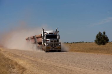 Central Queensland 'da tozlu, mühürsüz yolda ilerleyen üç karavanı olan bir tır..