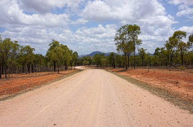 Kuzey Queensland, Avustralya 'da çalılıkların arasından tepelere uzanan boş bir volkanik kırmızı çakıl yolu.. 
