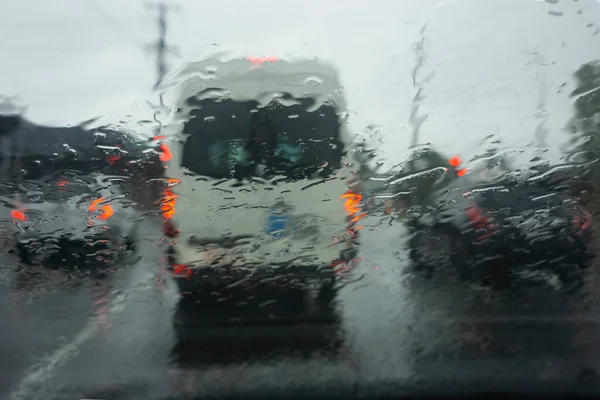 Traffic stopped at lights in the pouring rain in the early evening seen through the wet windscreen of a car.