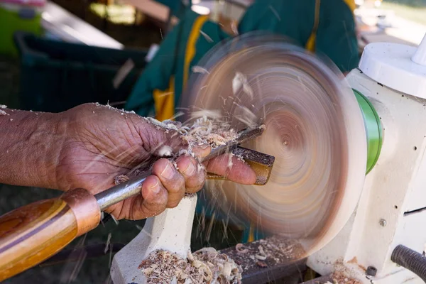 Man with a chisel turning a wooden bowl on a wood lathe with shavings flying off the work as it spins.