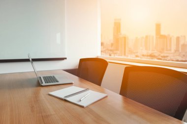 Laptop ve Not defteri üzerinde kalem için yapılacak işler tablo arka plan üzerinde cityscape manzaralı boş kurumsal konferans salonunda devam etti. Not Defteri seçili odak.