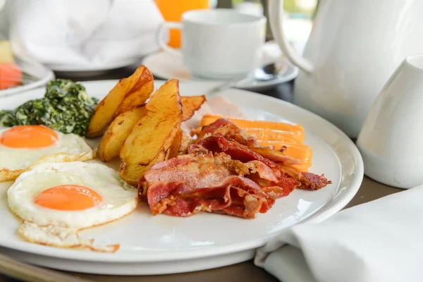 El desayuno consta de huevos, tocino, salchicha, tocino, patata y espinacas con queso. delicioso en la mañana — Foto de Stock