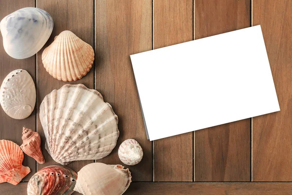 Вид сверху на различные морские ракушки с пустой белой бумагой на деревянном фоне. Летнее время — стоковое фото