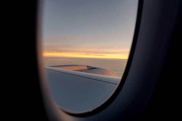 Вид из окна самолета, летящего над облаками на закате
