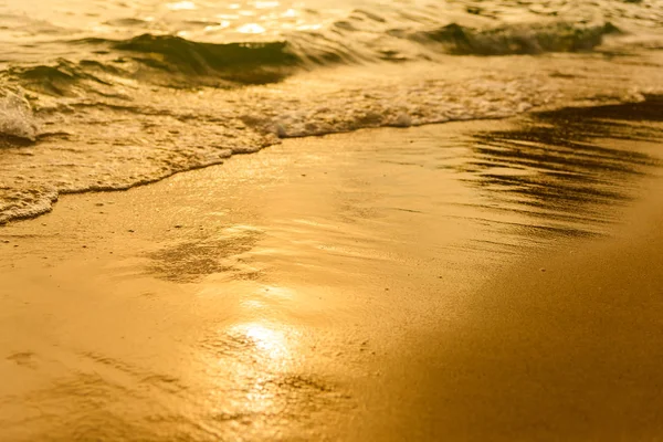 Goldenes Licht, das eine Wasserwelle am Meer und Sand bei Sonnenuntergang reflektiert. reines Gold — Stockfoto