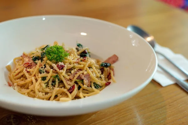 Herkullinen mausteinen spagetti pekonilla, kuivattu chili, basilika ja valkosipuli haarukalla ja lusikalla valmistella lisukkeita — kuvapankkivalokuva