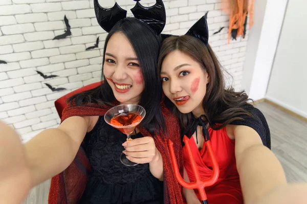 两名身穿巫婆服装 手持鸡尾酒眼镜 手持手机自拍自拍的亚洲美女的画像 — 图库照片