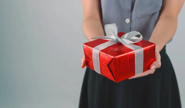 Red gift box with ribbon in hands woman for giving in holidays or celebration day with copy space for text. Holiday concept.