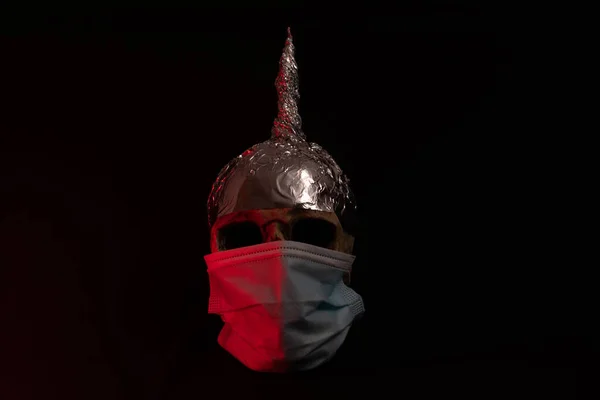 skull wearing surgical mask and a tinfoil hat, black background with red light