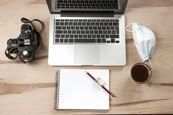 Maskeli, kalemli, kameralı ve kahveli bir fotoğrafçı ve bilgisayar tasarımcısının çalışma masası.