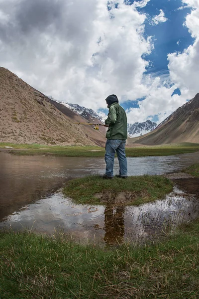 Yeşil ceketli bir adam dağlarda balık tutuyor.