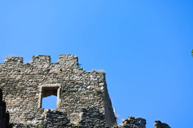 Yıpranmış taş duvarlar, bulutsuz, parlak mavi gökyüzüne karşı yükselir..