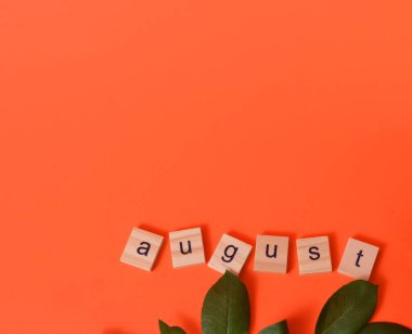 Turuncu arka planda yeşil yapraklar. Augustus ayı ahşap harflerle yazılmıştır. Takvim. Yaz.