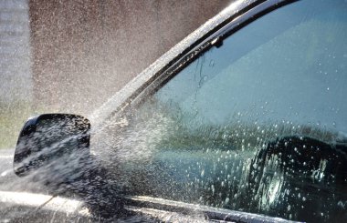 Şampuanla yıkanmış siyah bir araba. Arabanın camına su dökülüyor..