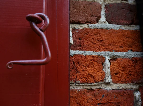 Detail of a red window shutter and a red brick wall beside. Hook to close the shutter.