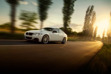 Engels, Rusya - 04 Haziran 2018: Beyaz araba Bmw 3 Serisi F30 boş kırsal asfalt yolda günbatımında kullanıyor