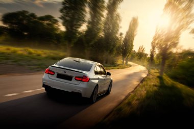 Engels, Rusya - 04 Haziran 2018: Beyaz araba Bmw 3 Serisi F30 boş kırsal asfalt yolda günbatımında kullanıyor