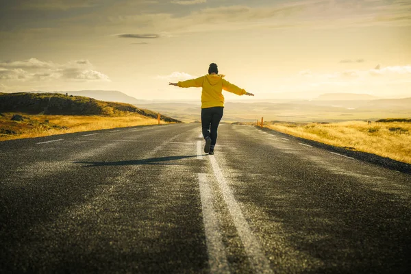 Iceland road trip. Girl is walking alone on road to sunset and keeping balance on dividing strip line. Freedom concept. Beautiful icelandic landscape