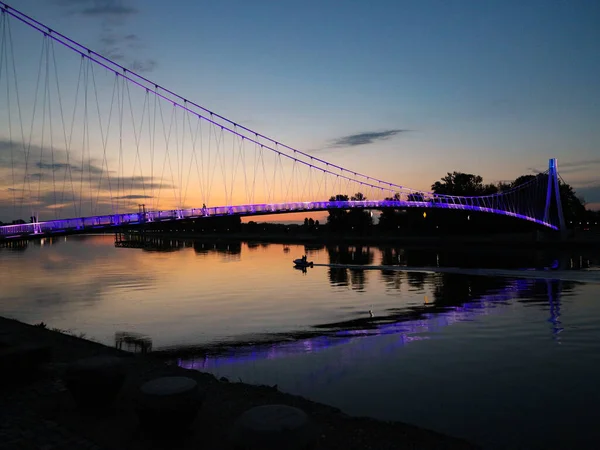 Osijek / Hırvatistan-18 Haziran 2019: Harika askıya alınmış yaya köprüsü Drava Nehri 'ni geçiyor, gece karanlığında ışıklarla aydınlanıyor                         