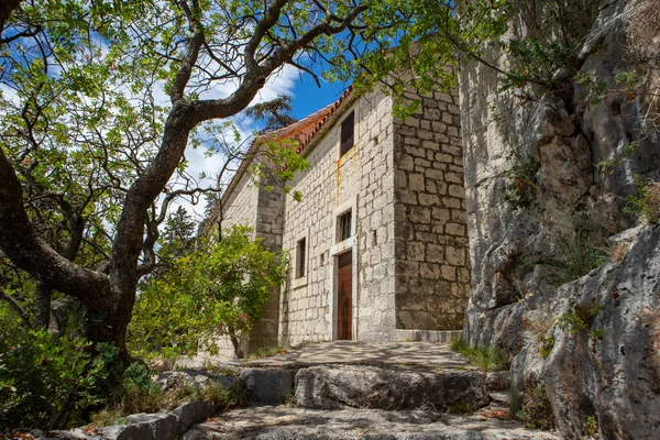 Ciovo, Hırvatistan-21 Haziran 2020: Ciovo adasının güney tarafındaki taş kilise mabedi, çam ağacı ormanında dik, devasa kayalıkların altına inşa edildi.